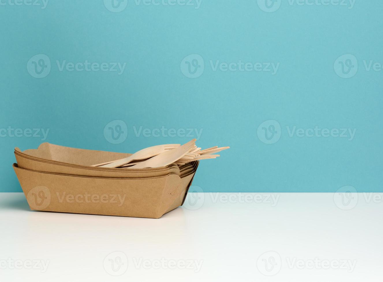 disposable paper rectangular plates, wooden forks and knives on white table, blue background photo