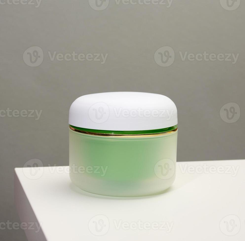 green jar for cosmetics on a white table. Packaging for cream, gel, serum, advertising and product promotion, mock up photo