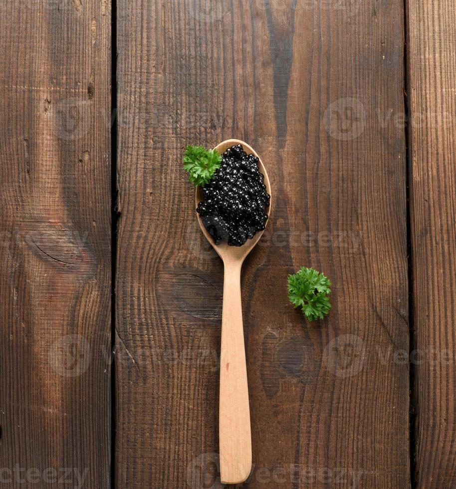 fresh grainy black paddlefish caviar in brown wooden spoon on a black background, top view photo