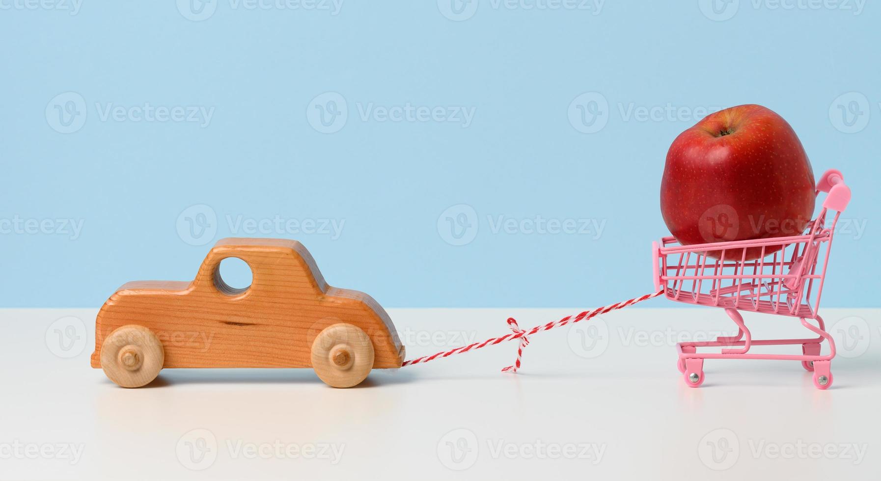 a wooden children's machine pulls a miniature iron shopping cart with an apple on a rope. photo