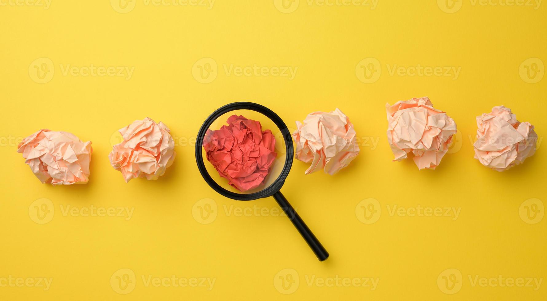 bolas de papel arrugadas y lupa de plástico negro sobre un fondo amarillo. concepto de búsqueda de ideas y soluciones foto