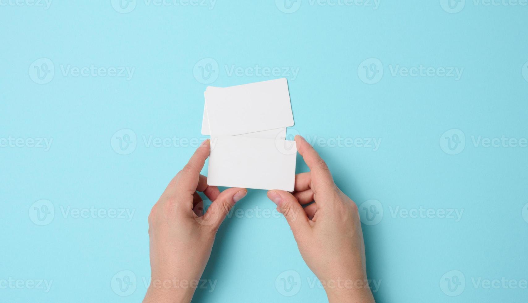 Female hand holding empty paper white business card on a blue background. Copy space photo