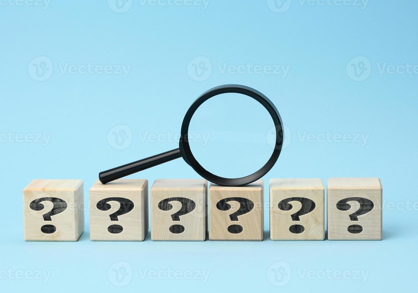 wooden cubes with question marks and a magnifying glass on a blue background photo