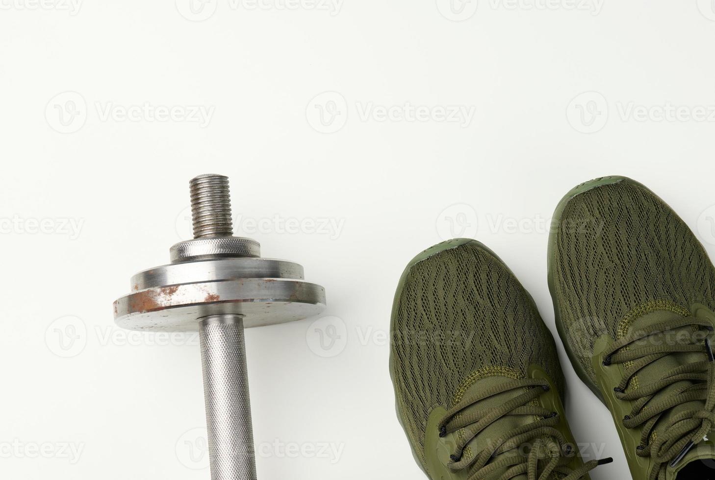 pair of green textile sneakers and a metal dumbbell on a white background, top view. photo