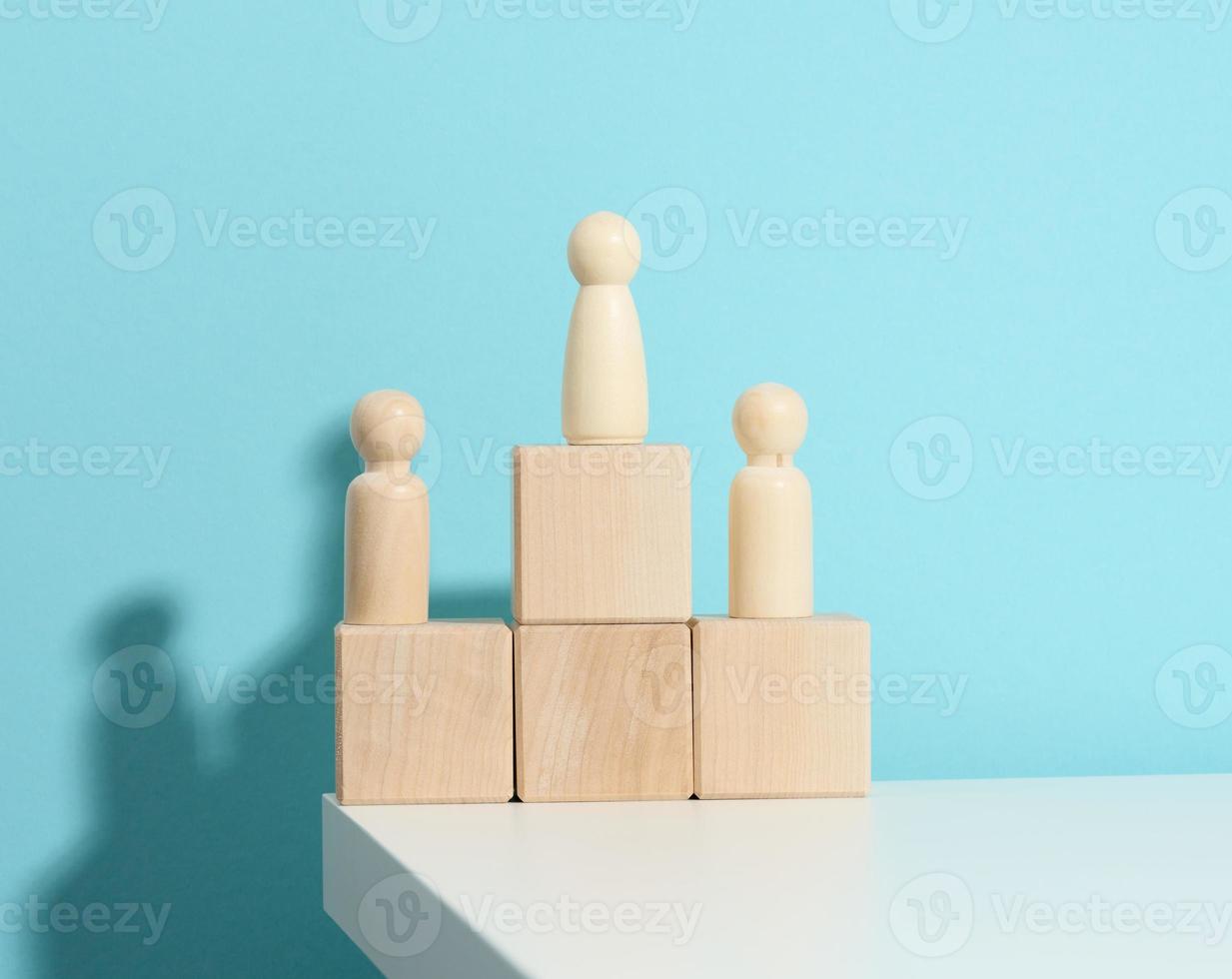 wooden figures of men stand on a pedestal of their cubes on a blue background. The concept of rivalry in sports, business and life. Achieving success and leadership photo