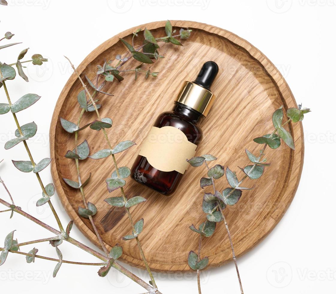 brown glass bottle with a pipette and an empty glued label on a wooden board, next to a branch of eucalyptus photo