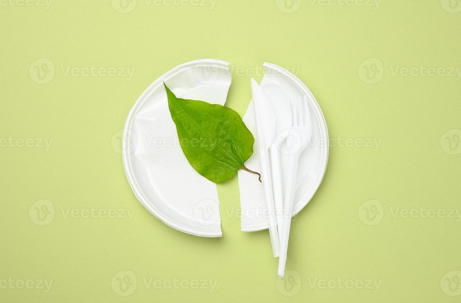 broken white plastic plate and green leaf on a green background. The concept of avoiding plastic, preserving the environment photo