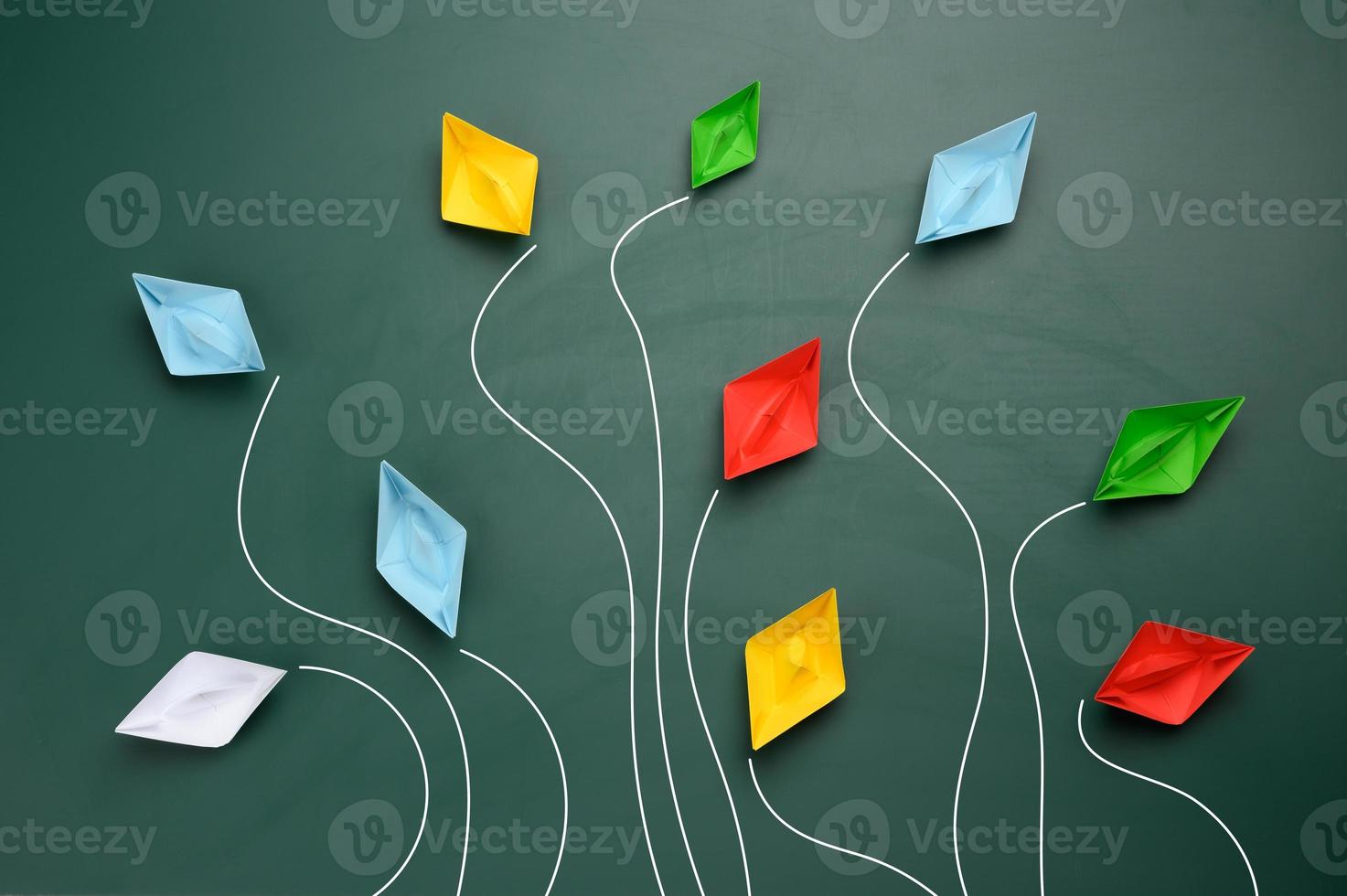 a group of multi-colored paper boats flies in different directions on a green background photo