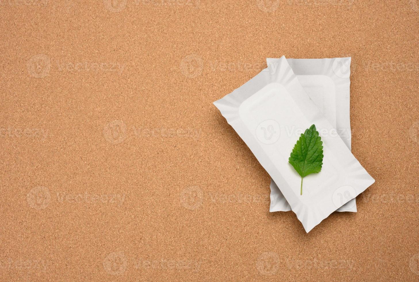 rectangular white paper plates and a green leaf on a brown cork background. No plastic concept, top view photo