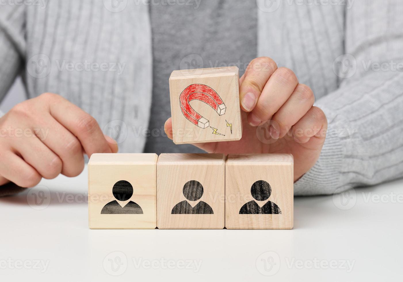 la mano femenina sostiene un cubo de madera con un imán sobre los cubos con hombres pequeños, reclutando para un equipo fuerte. vacantes abiertas en la empresa foto