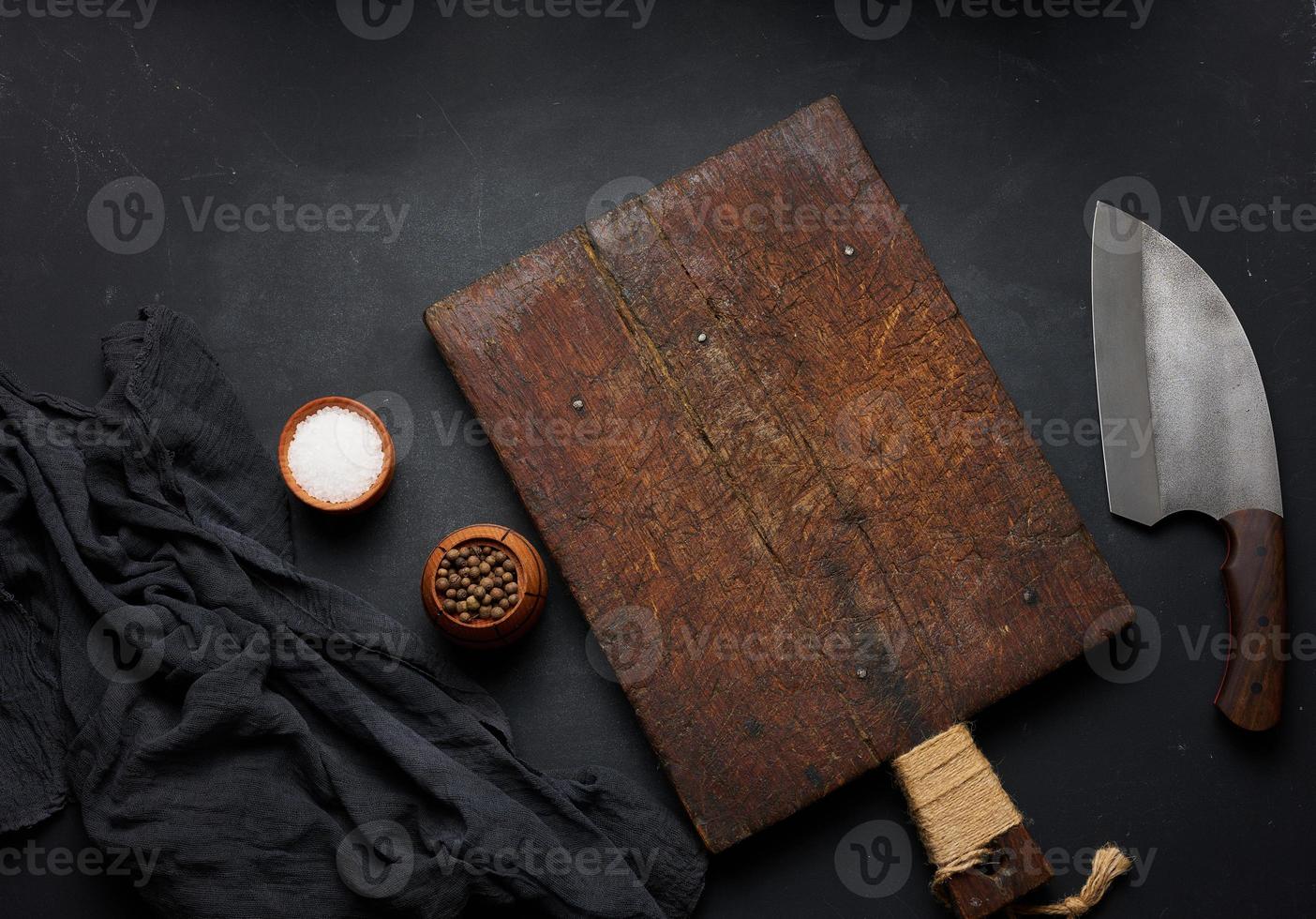 Rectangular empty wooden cutting board and kitchen knife on black table with gauze napkin, top view photo