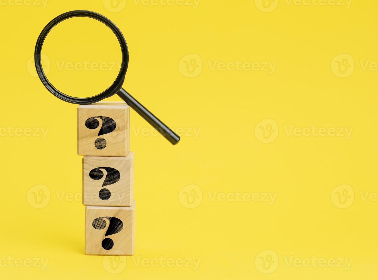 wooden cubes with question marks and a magnifying glass on a yellow background. The concept of finding answers to unknown questions photo