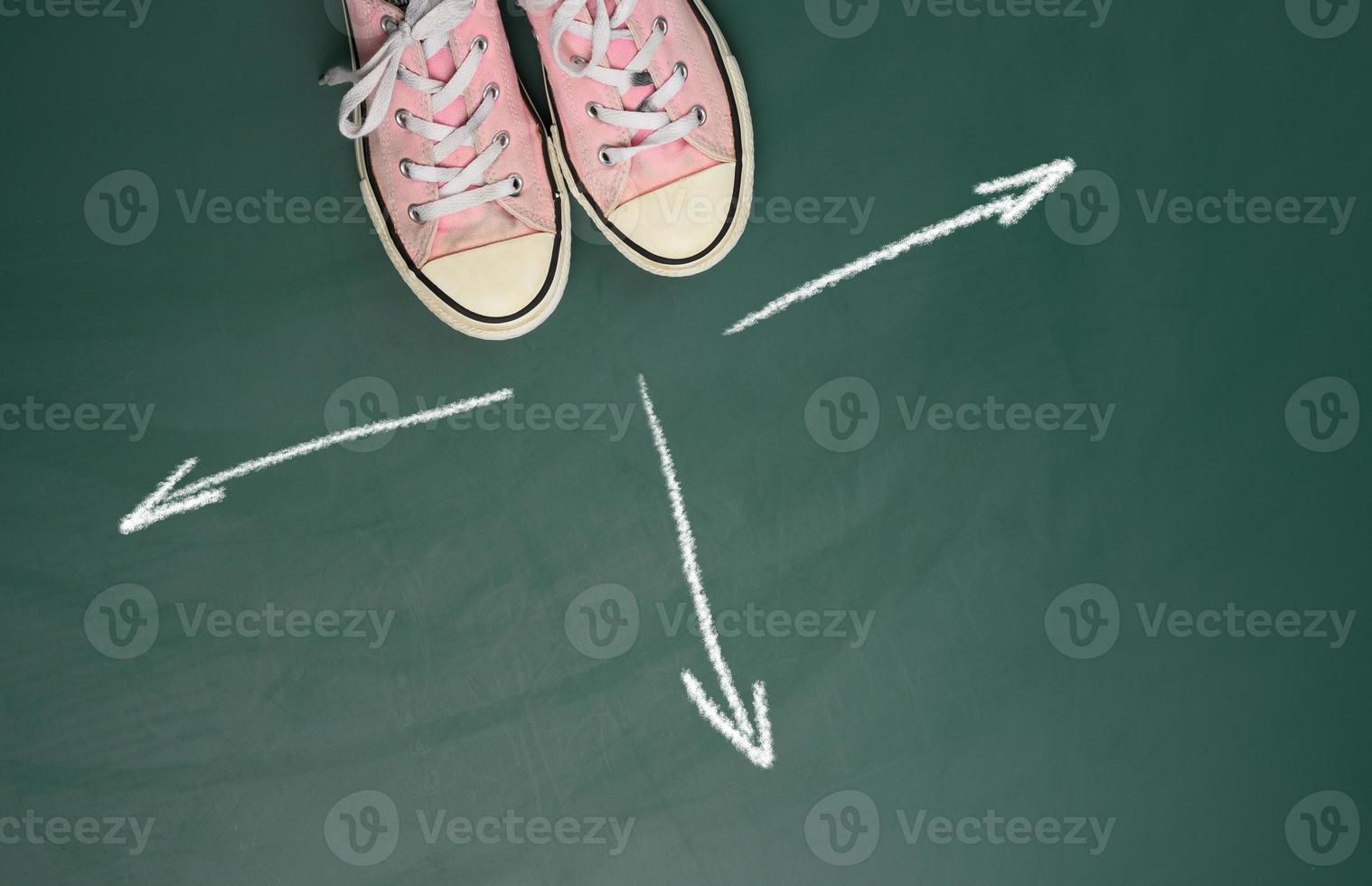 pair of pink sneakers on a green background and arrows drawn in equal directions in white chalk photo