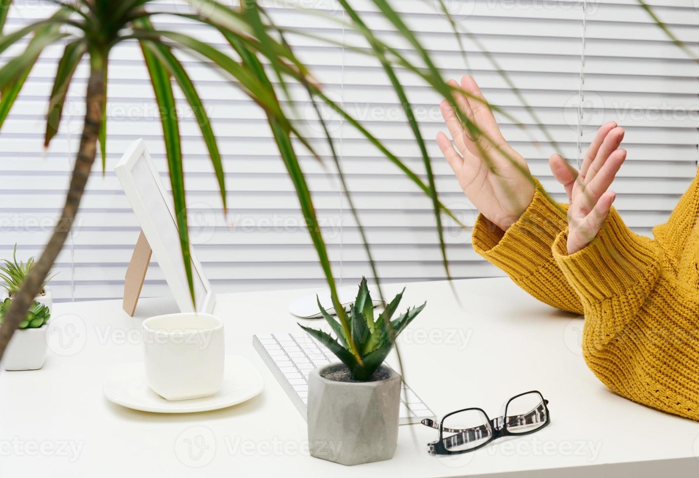 woman sits at a white desk and gestures with her hands, video call and conversation photo