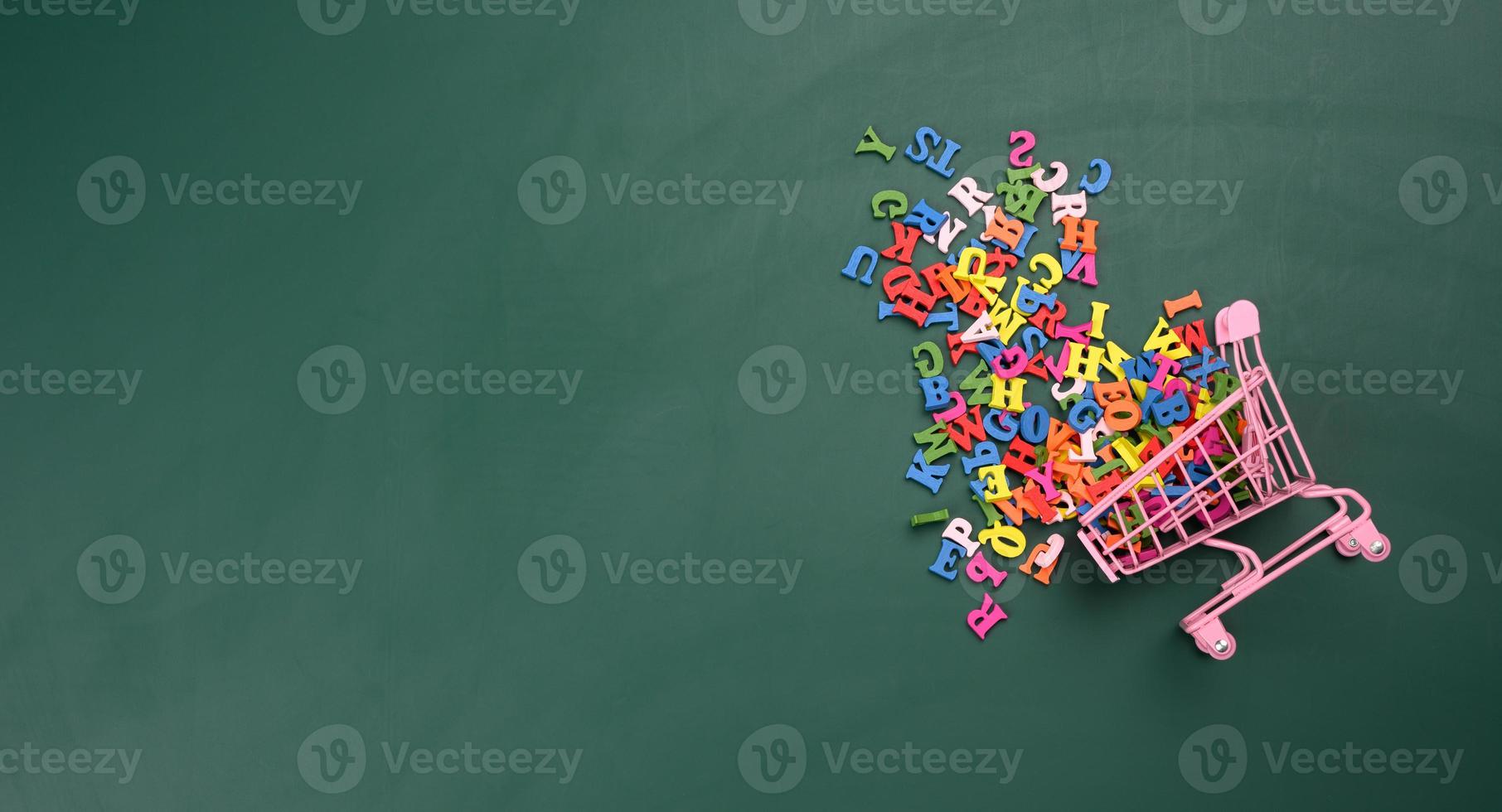 scattered multicolored letters of the english alphabet from a miniature shopping cart on a green background photo