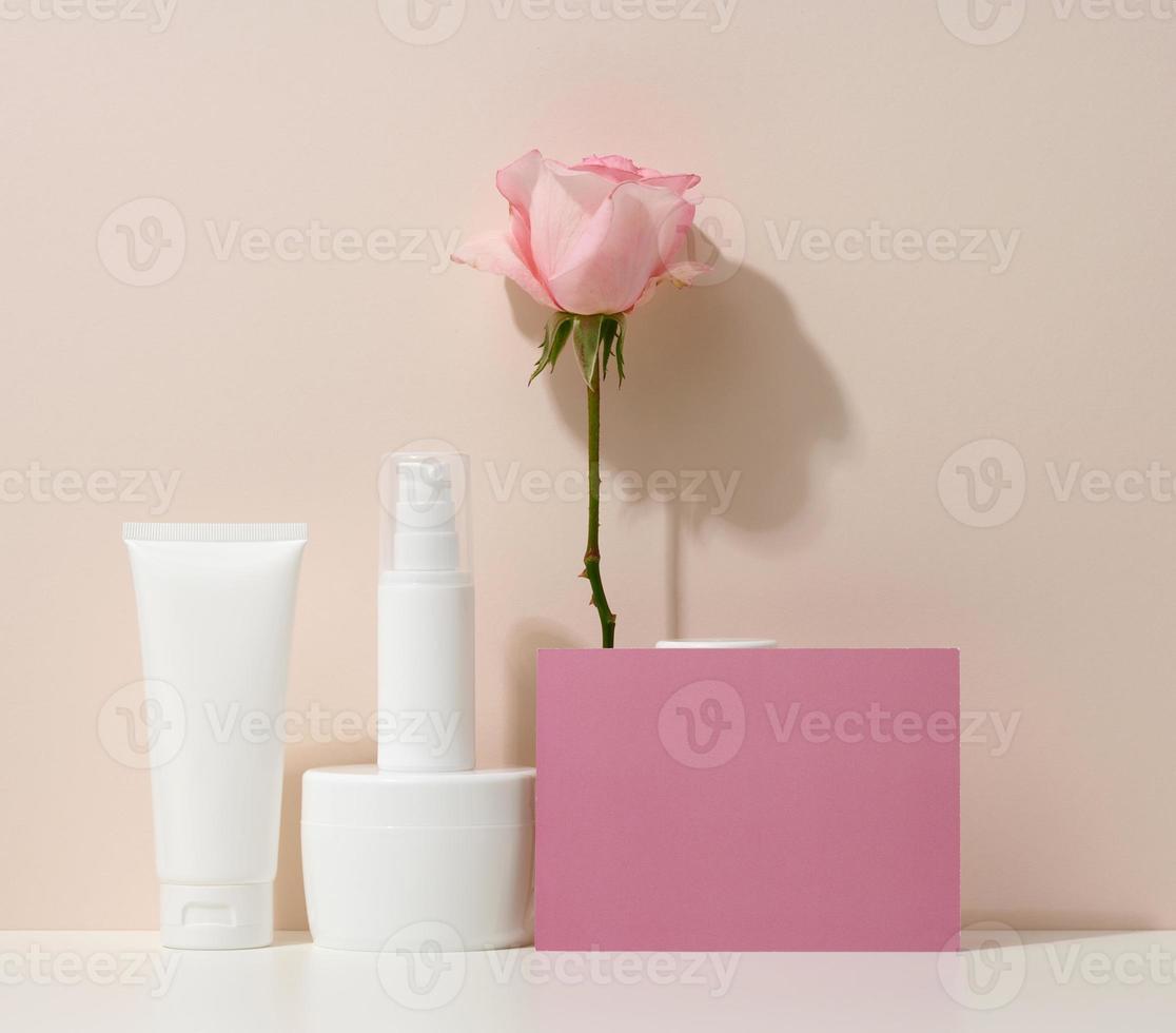 blank cardboard business card and a set of jars, tubes and plastic bottles on a beige background. Cosmetic branding, promotion and advertising photo