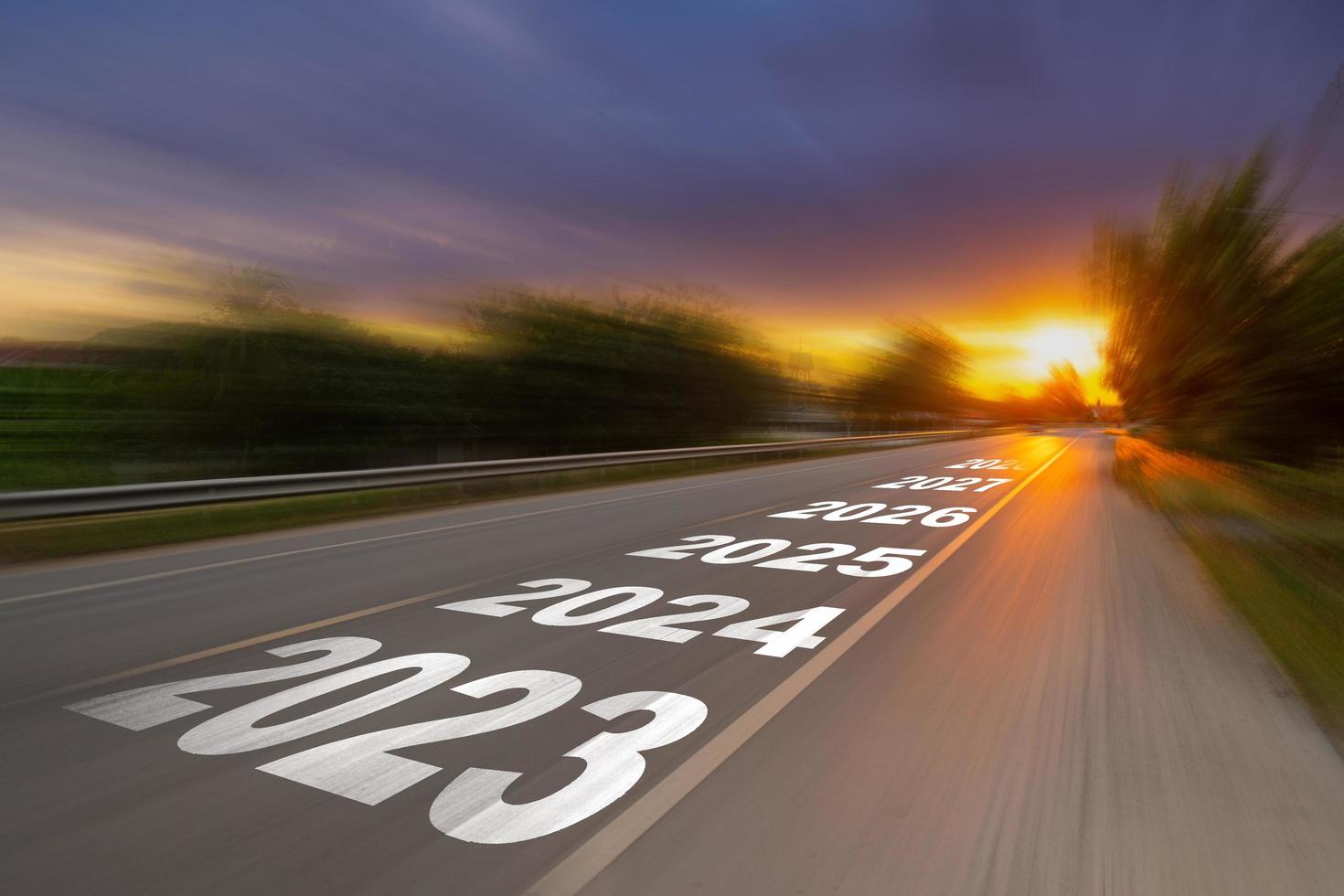 desenfoque de movimiento carretera asfaltada vacía y concepto de año nuevo 2023. conduciendo por una carretera vacía hacia los objetivos 2023 con puesta de sol. foto