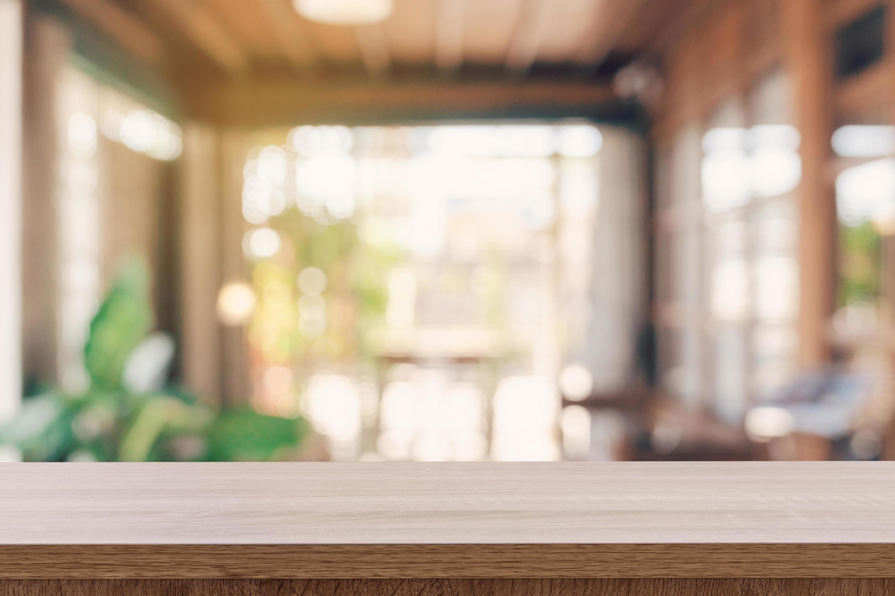 Wooden table top with blurred people in coffee shop and cafe background