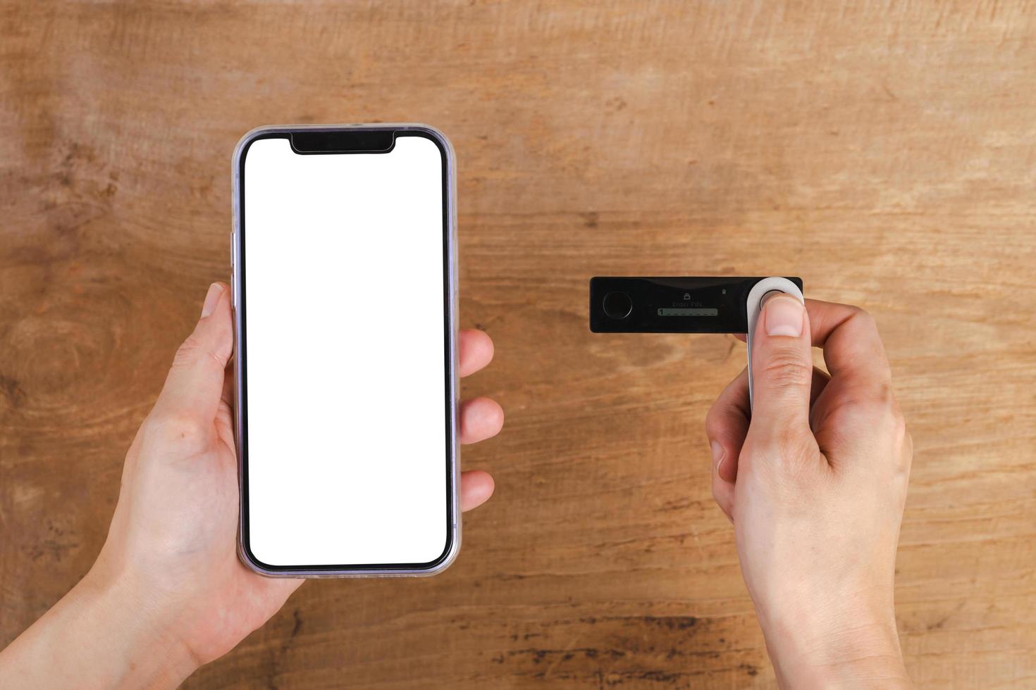 Hand holding mobile phone and hardware wallet on wooden table photo