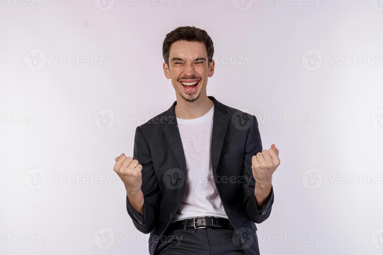 Portrait of happy joyful young businessman standing doing winner gesture clenching fists keeping isolated on white color wall background studio photo