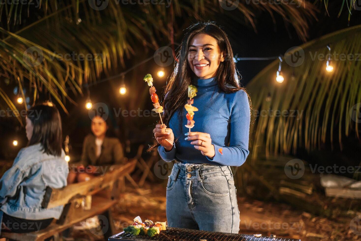 Portrait of Happy Asian young woman cooking meat on barbecue grill at new year party. Bar-B-Q or BBQ on traditional stove. Night Party, people and celebration concept. photo