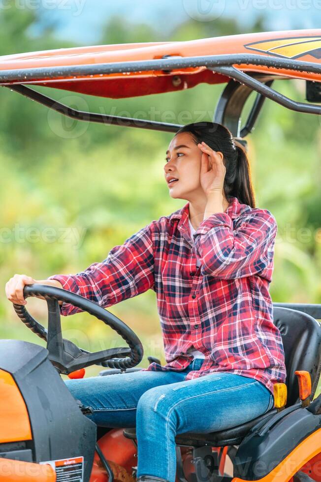 joven agricultora asiática sentada en una gran máquina tractora en tierras de cultivo. tecnologías modernas en gestión agrícola y concepto de agronegocios. foto