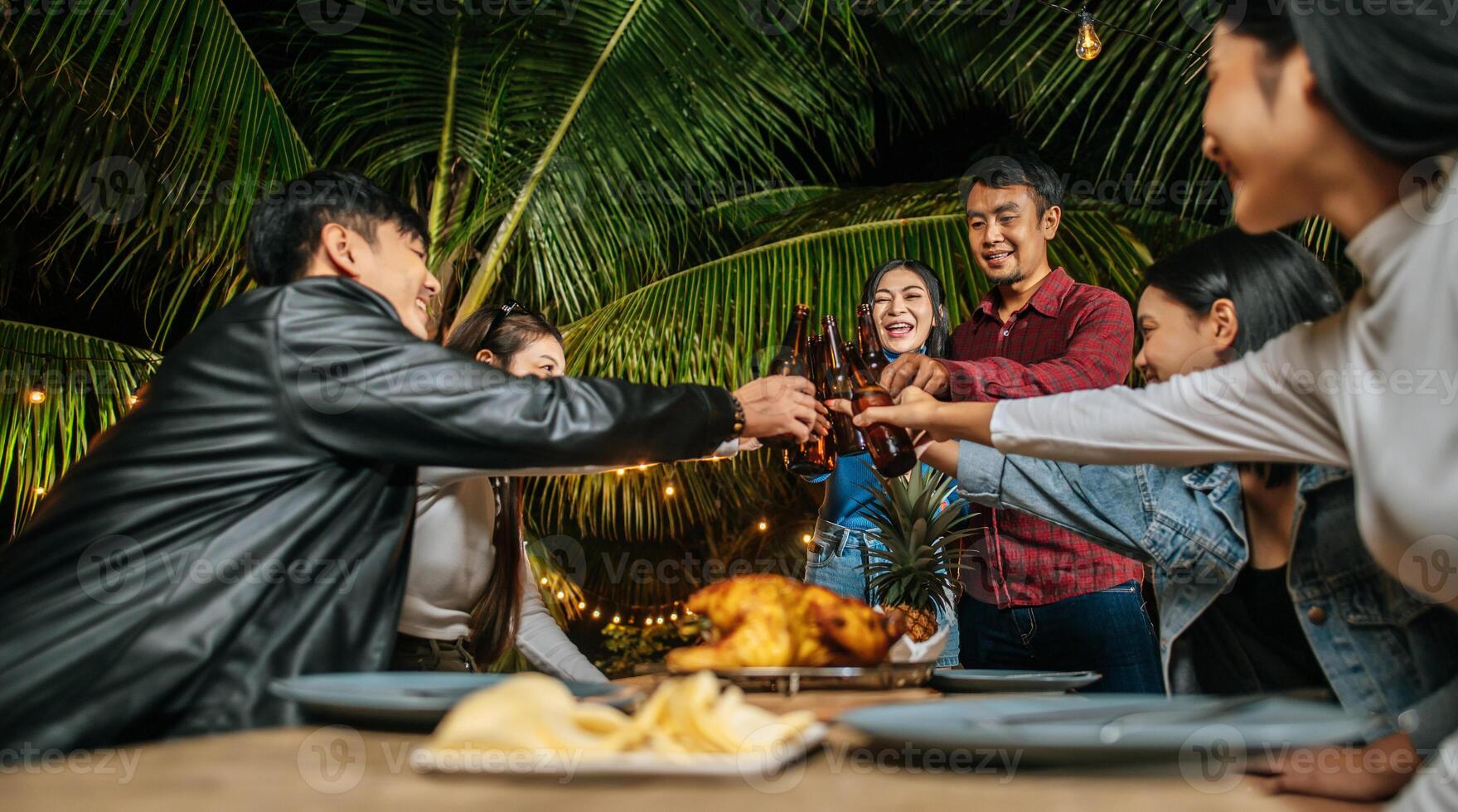 Portrait of Happy Asian friends having dinner party together - Young people sitting at bar table toasting beer glasses dinner outdoor  - People, food, drink lifestyle, new year celebration concept. photo