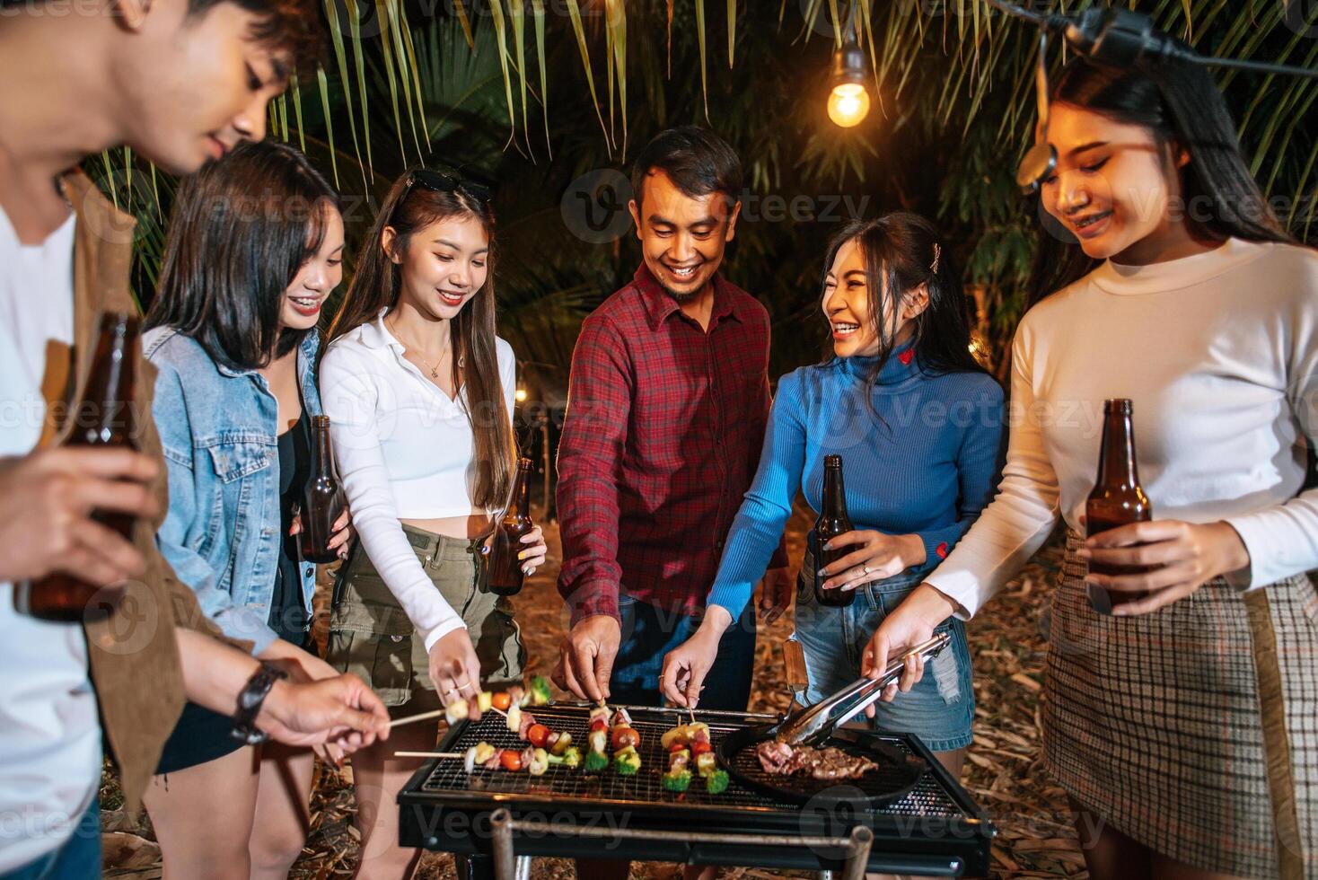 felices amigos asiáticos animando con una cena de barbacoa al aire libre - grupo de personas divirtiéndose en la fiesta de año nuevo. gente, comida y bebida concepto de estilo de vida fiesta nocturna, gente y concepto de celebración. foto