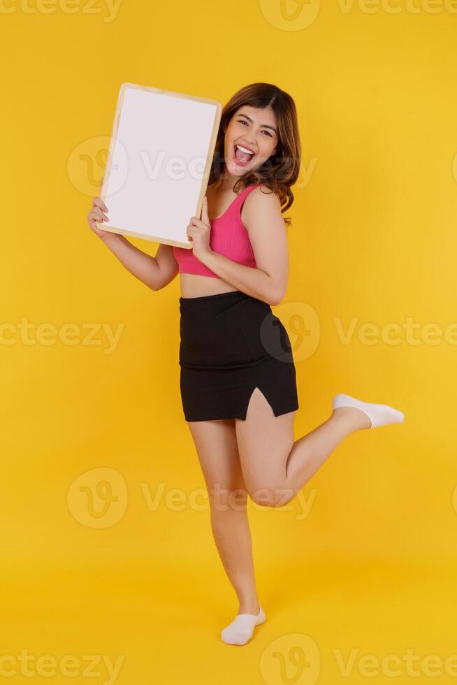 Portrait of Happy young woman holding an empty white placard over isolated yellow background. photo