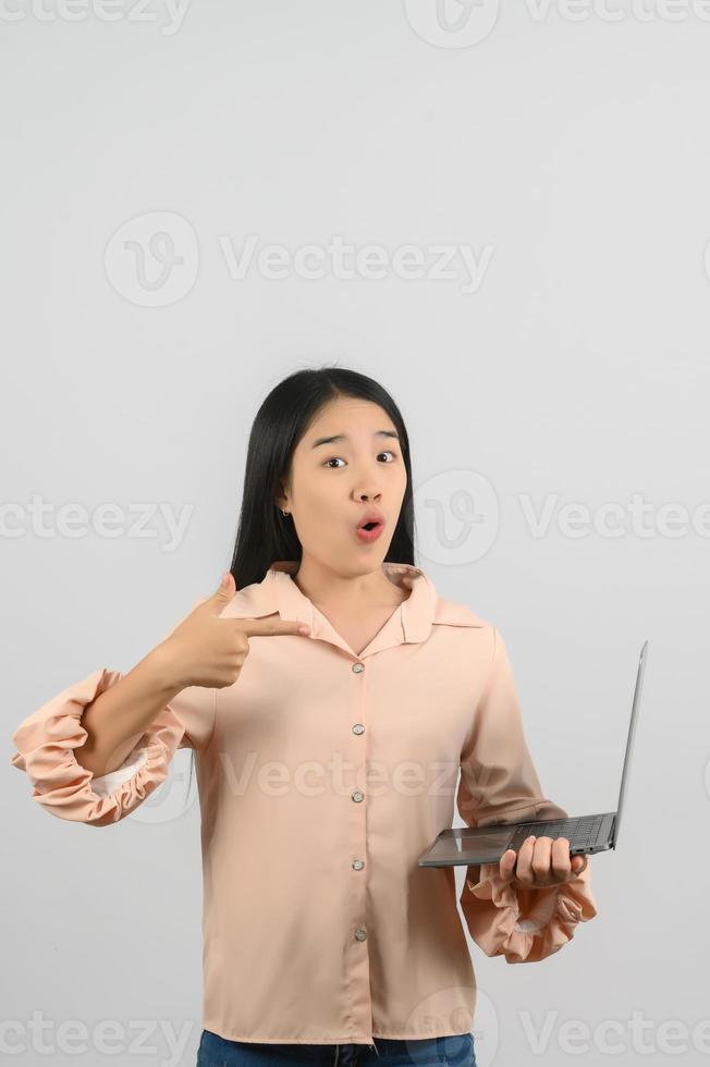 Portrait of Happy young woman holding laptop in her hands while standing isolated over yellow background. Technology and Business concept. photo