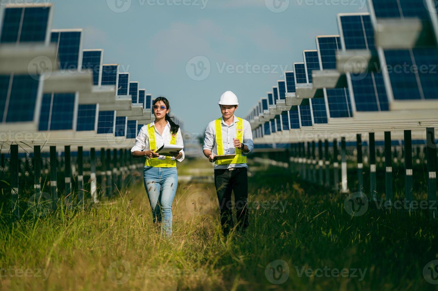 joven inspector asiático ingeniero hombre y mujer caminando comprobando la operación en una granja solar foto
