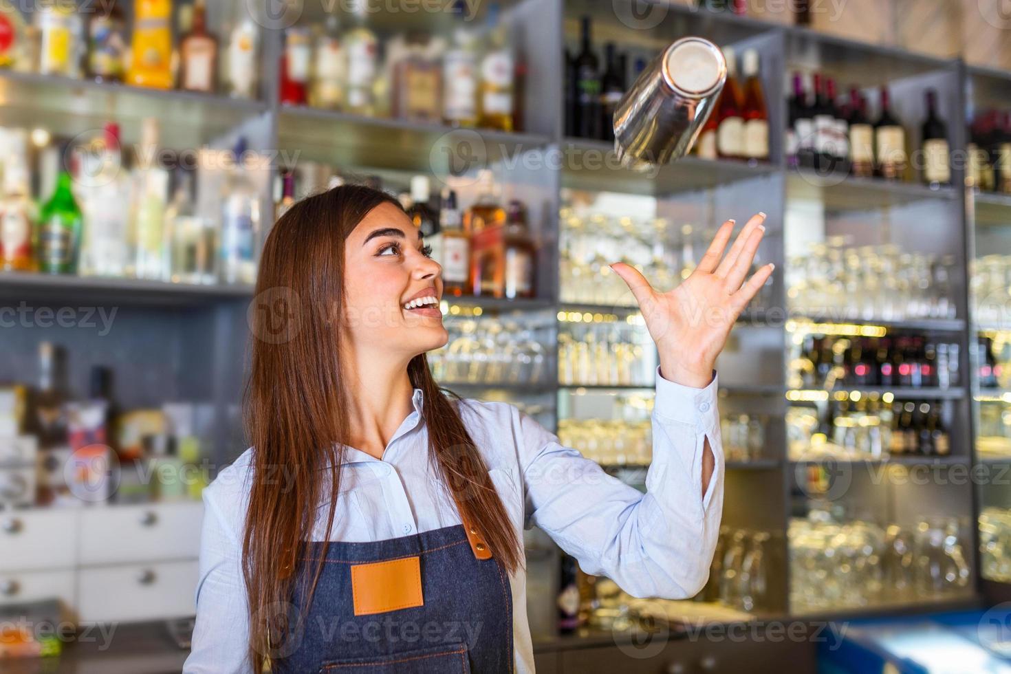 Beautiful female bartender tosses cocktails shaker into the air and arranges a real show for their guests. photo