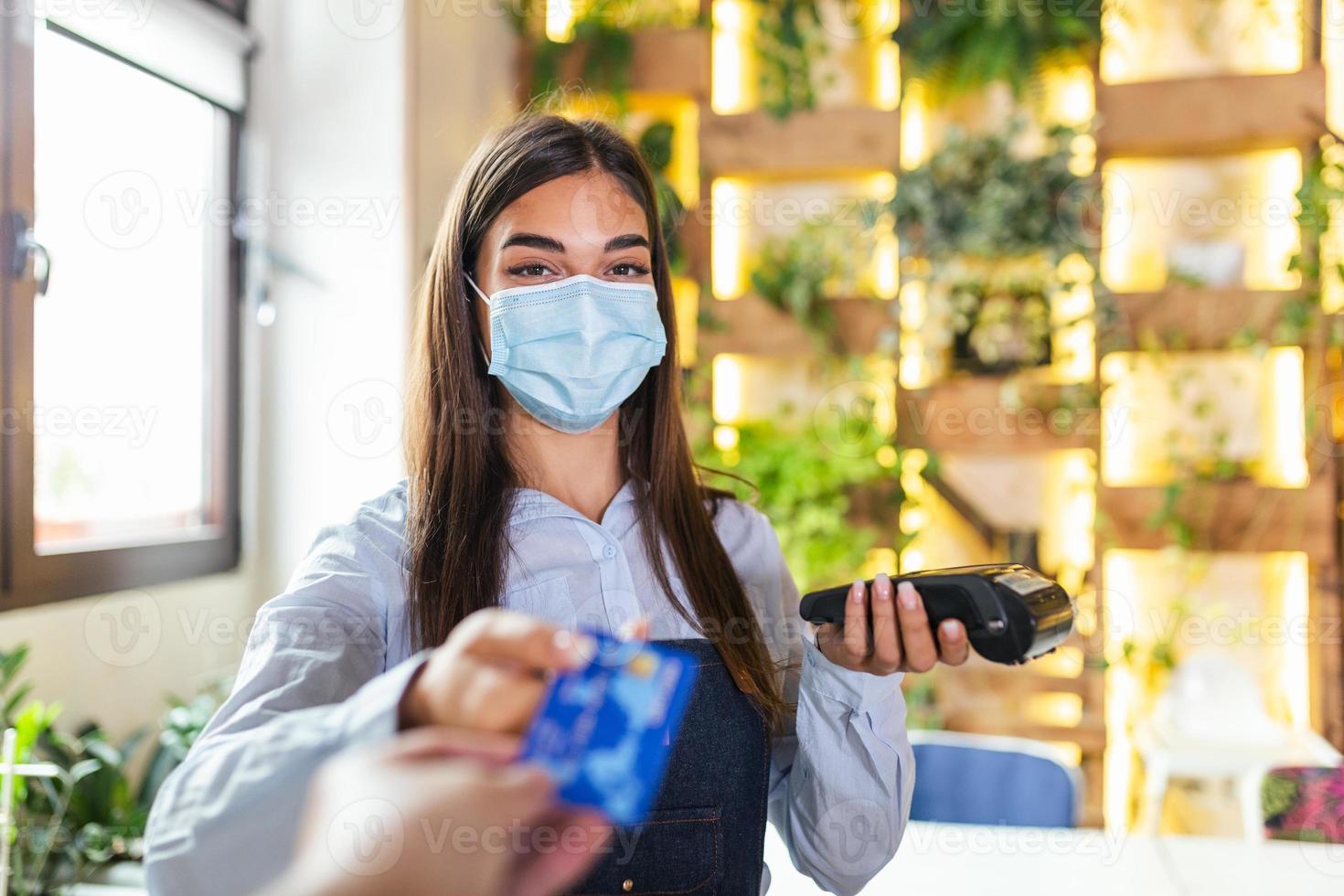 Waitress holding credit card reader machine and wearing protective face mask with client holding credit card. Man hand of customer paying with contactless credit card with NFC technology. photo