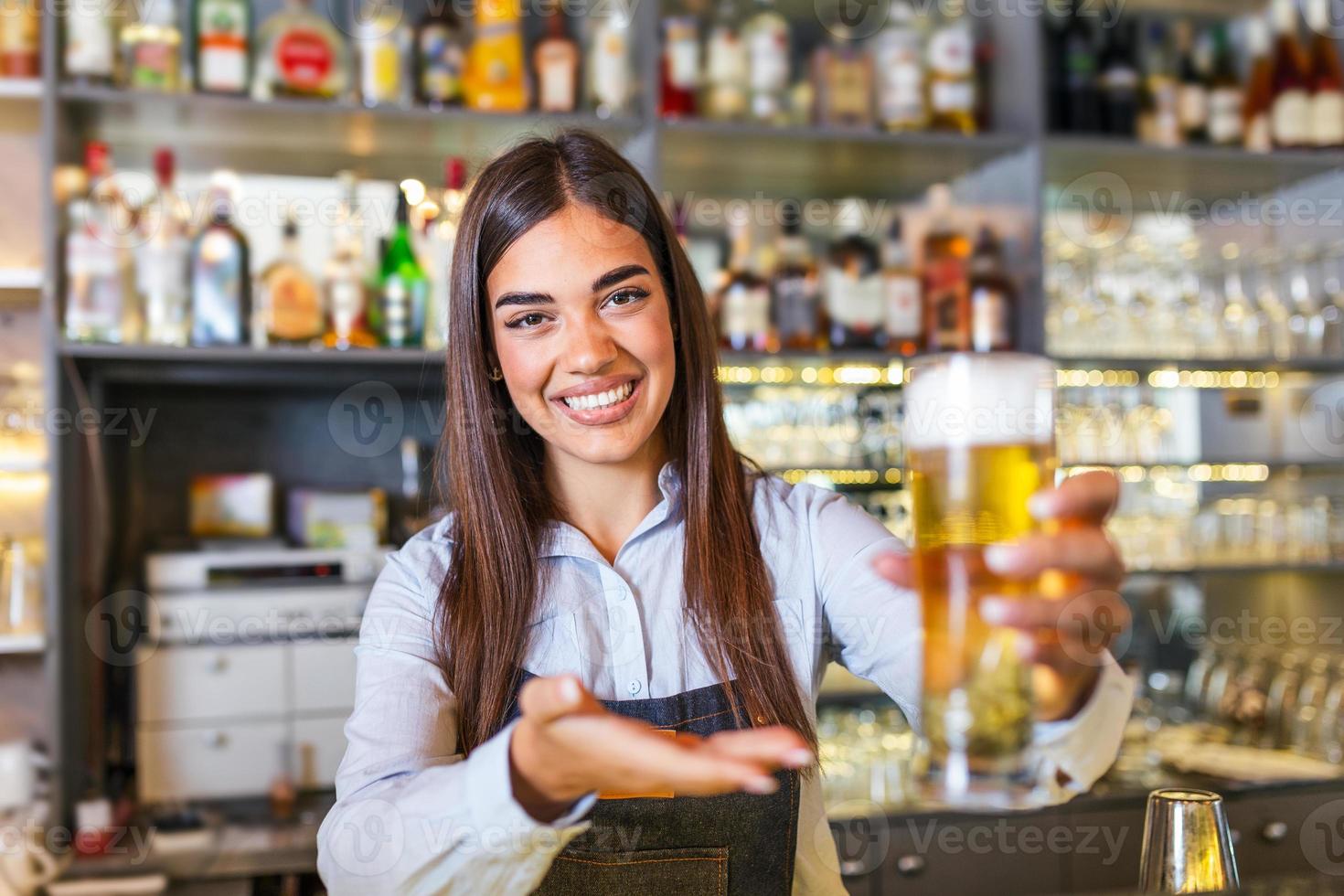 hermosa camarera sonriente que sirve una cerveza de barril en el mostrador del bar, estantes llenos de botellas con alcohol en el fondo foto