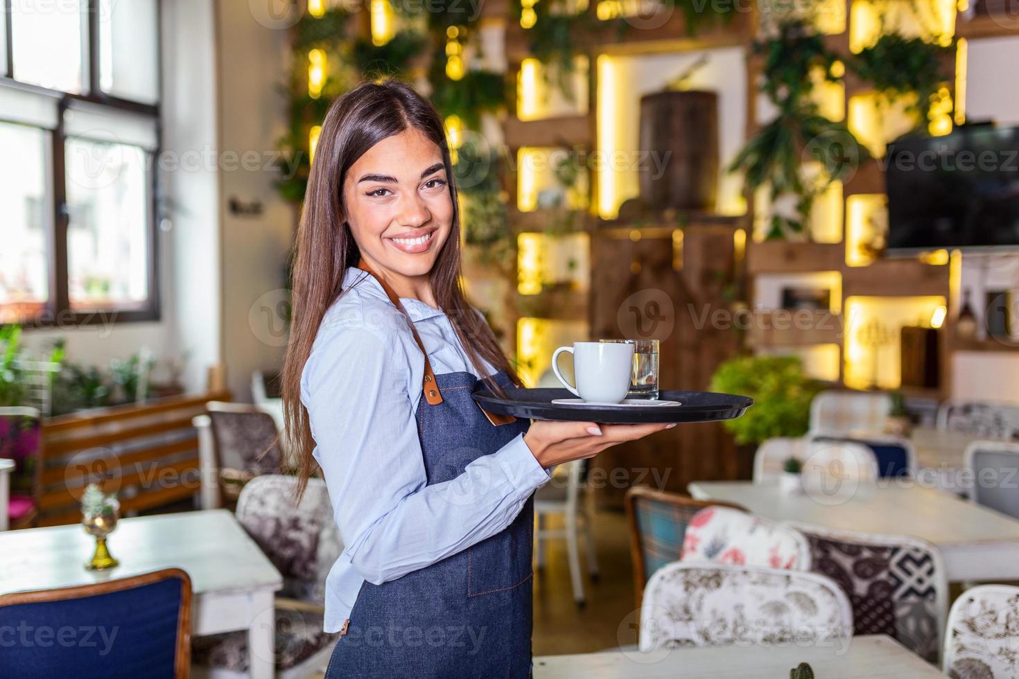 Happy waitress holding tray with cup of coffee, working in cafeteria and serves the table photo