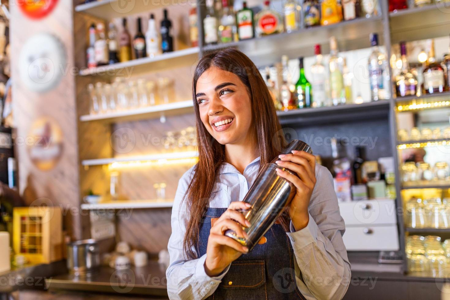 joven trabajadora en el mostrador de la camarera en el bar del restaurante preparando un cóctel con agitador. bella joven detrás de la barra haciendo un cóctel foto