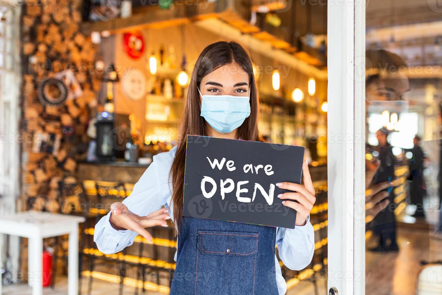 Small business owner with face mask holding the sign for the reopening of the place after the quarantine due to covid-19. Woman with protective mask holding sign we are open, support local business. photo