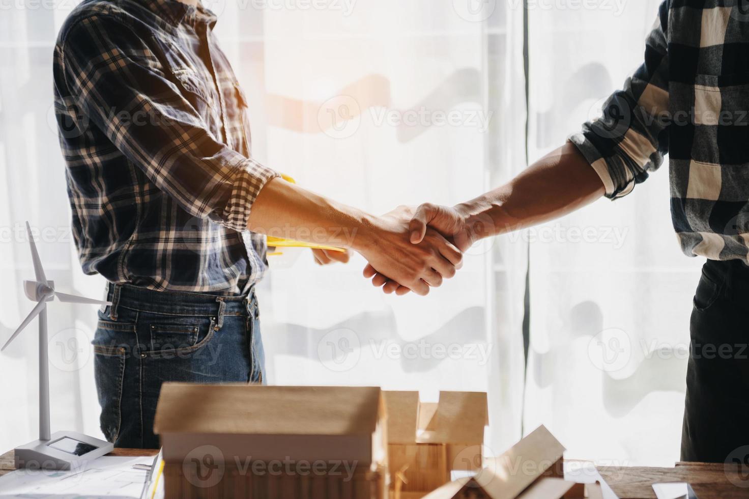 Engineers or architecture shaking hands at construction site for architectural project, holding safety helmet on their hands. photo