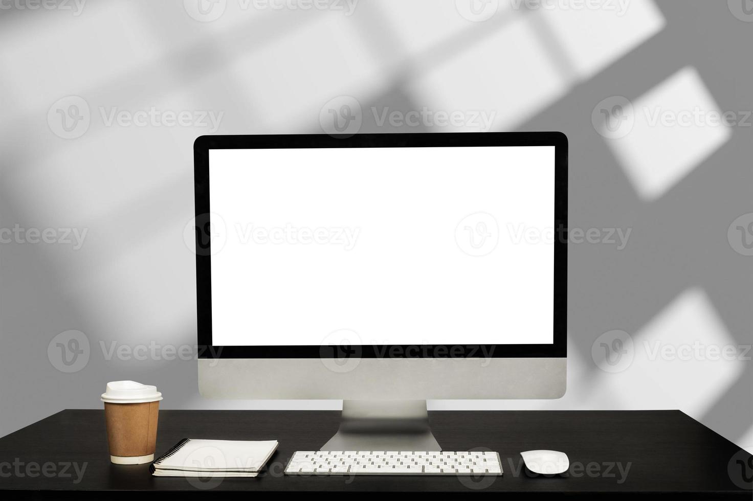 Computer monitor with white blank screen putting on white working desk with wireless mouse and keyboard over blurred modern office as background. photo