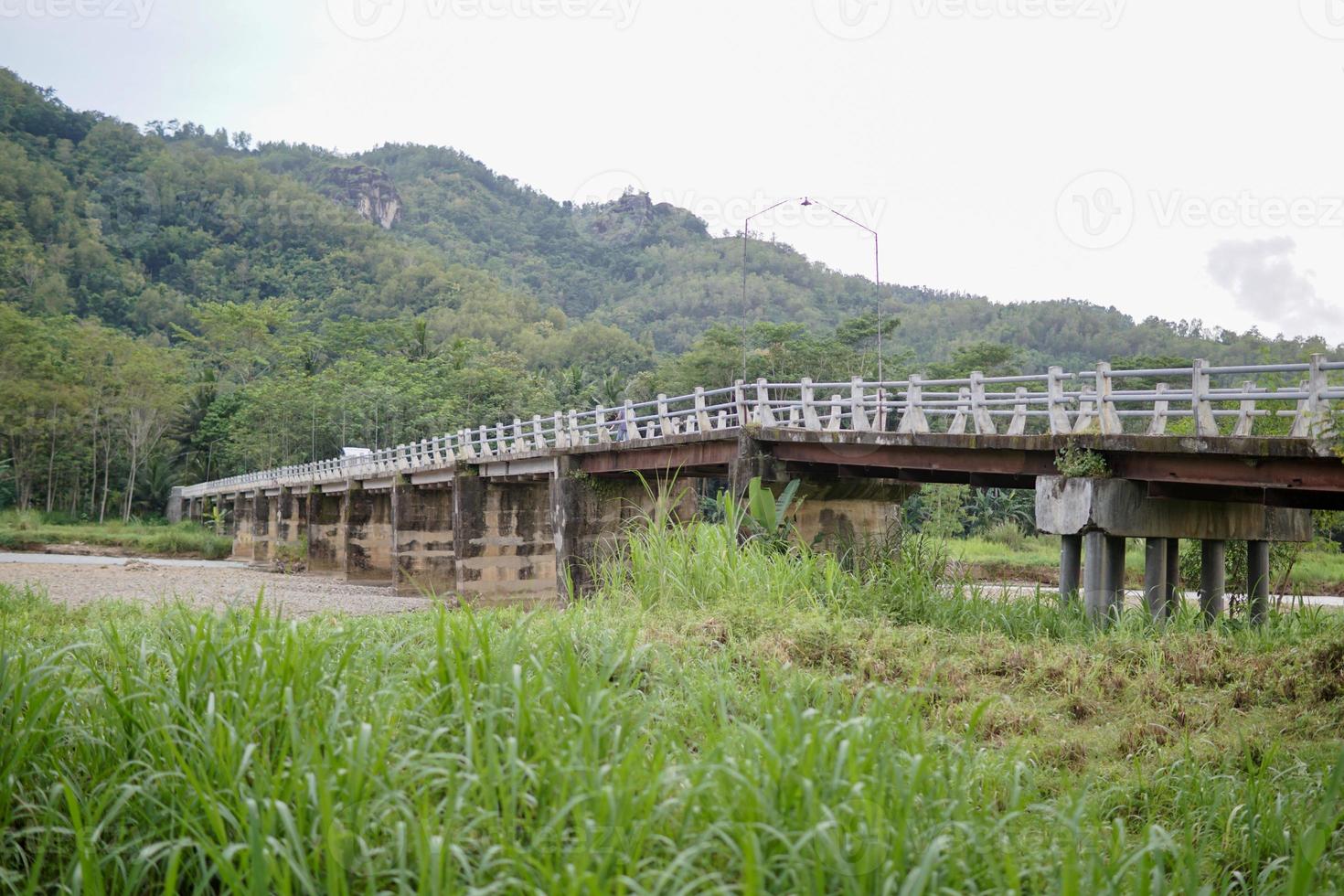 a bridge crossing people from village to village with a view of the river and green mountains photo