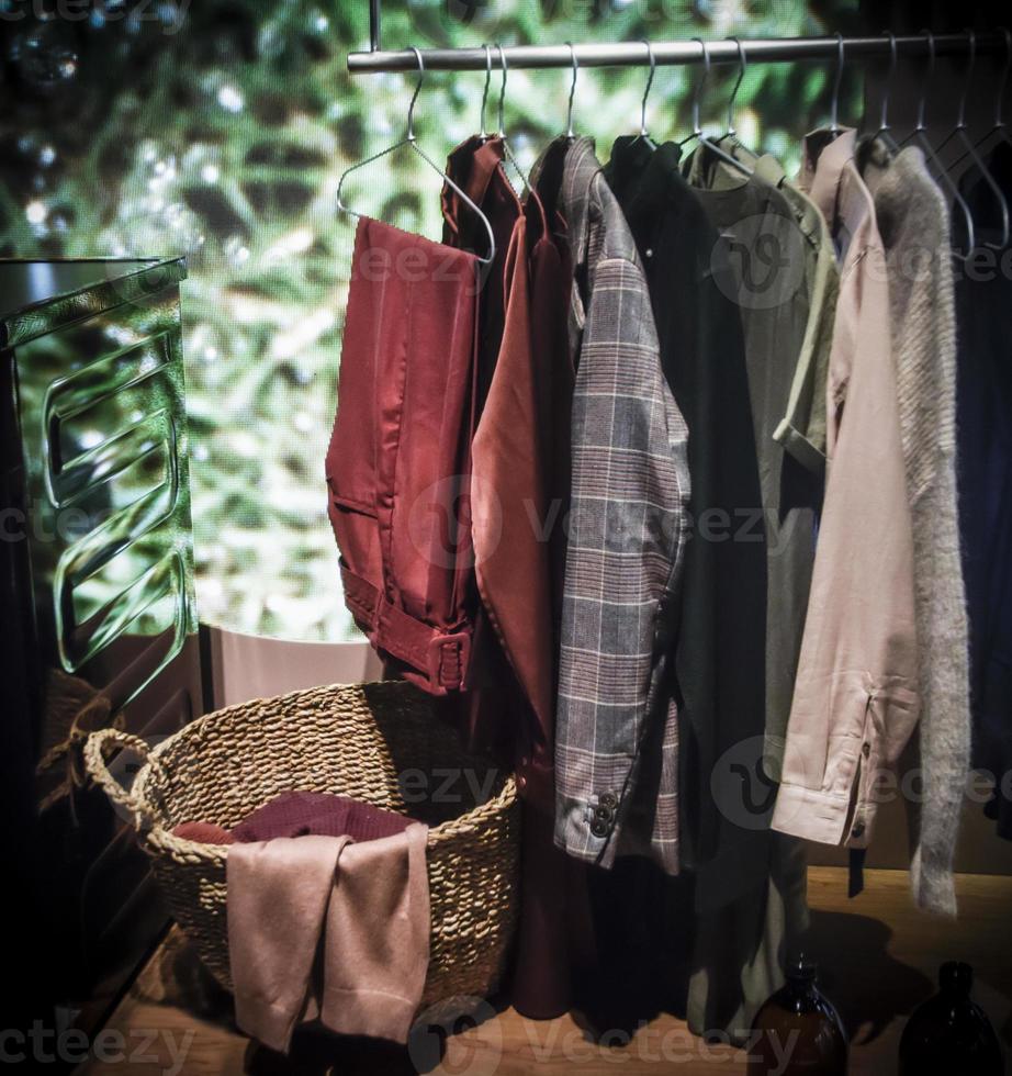 A row of multicolored clothes hanging next to a laundry basket photo