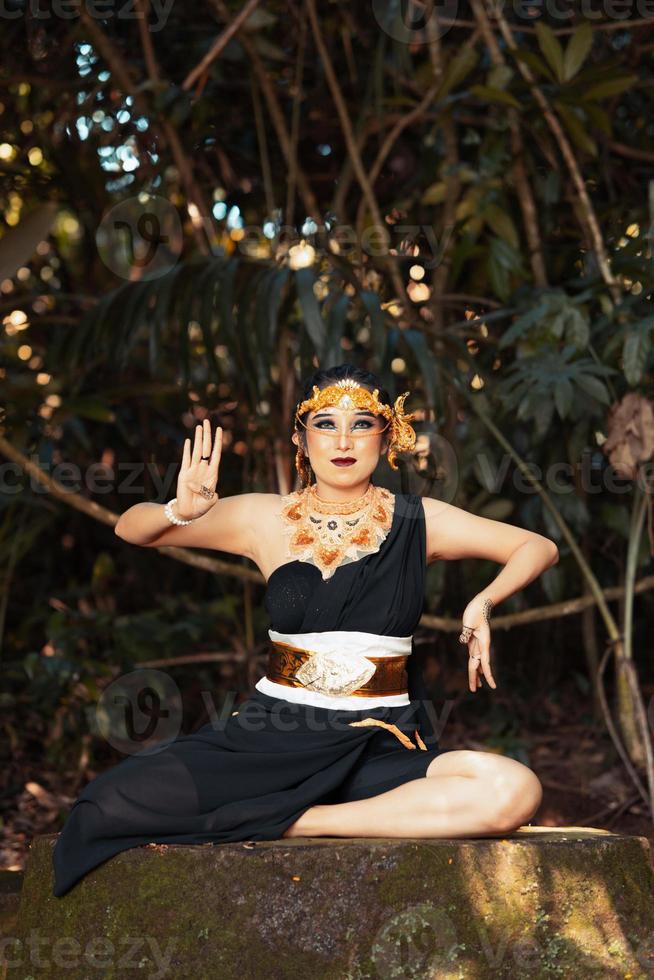 Indonesian woman sitting on the rock in a black dance costume while wearing a golden crown and golden necklace photo