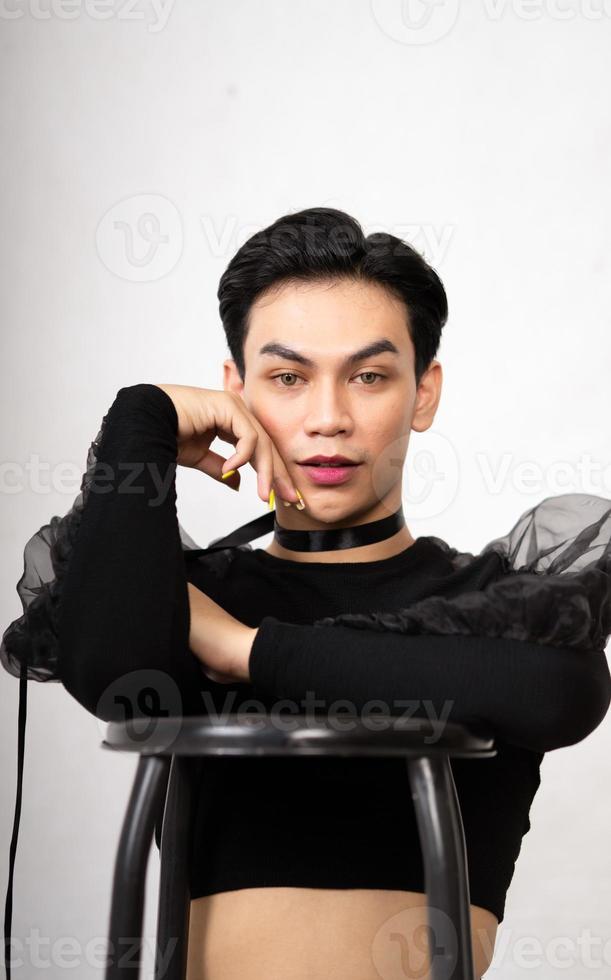 hermoso hombre asiático posando con la silla mientras usa un traje negro y maquillaje foto