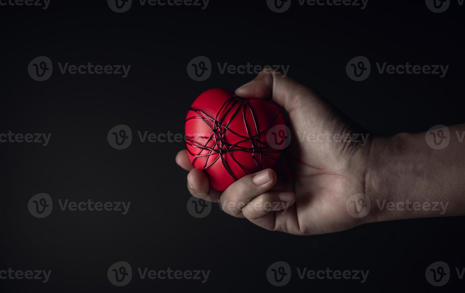 concepto doloroso, tristeza, falta de libertad. mucha angustia y tristeza. mano sosteniendo y apretando un corazón rojo con alambre de cobre desordenado atado. tono oscuro foto