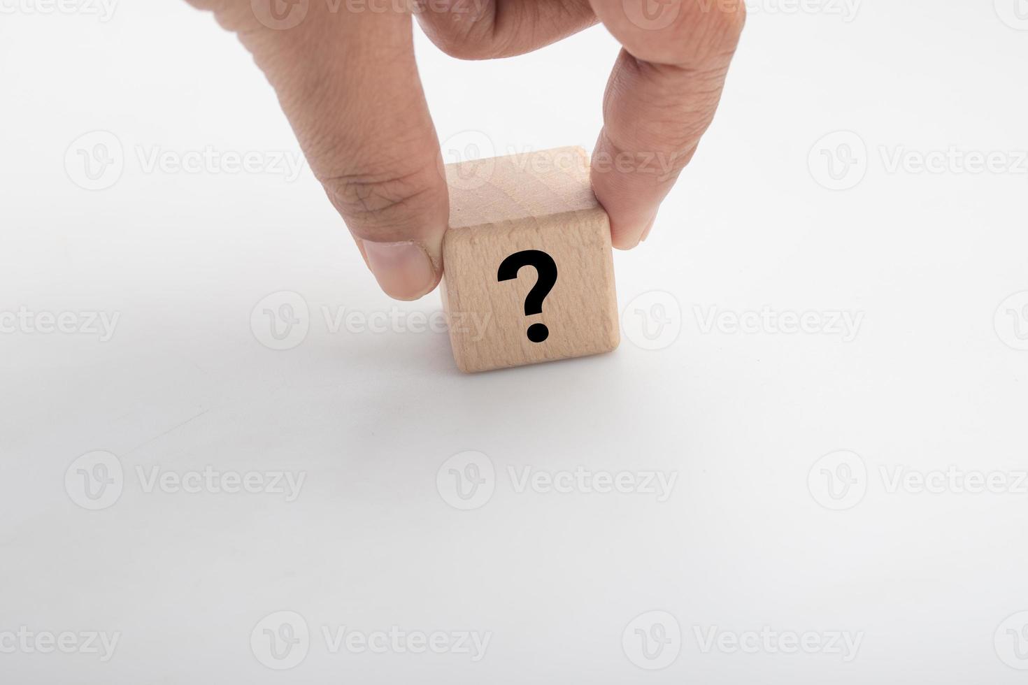 Hand holding a wooden block with a question mark on a white background photo
