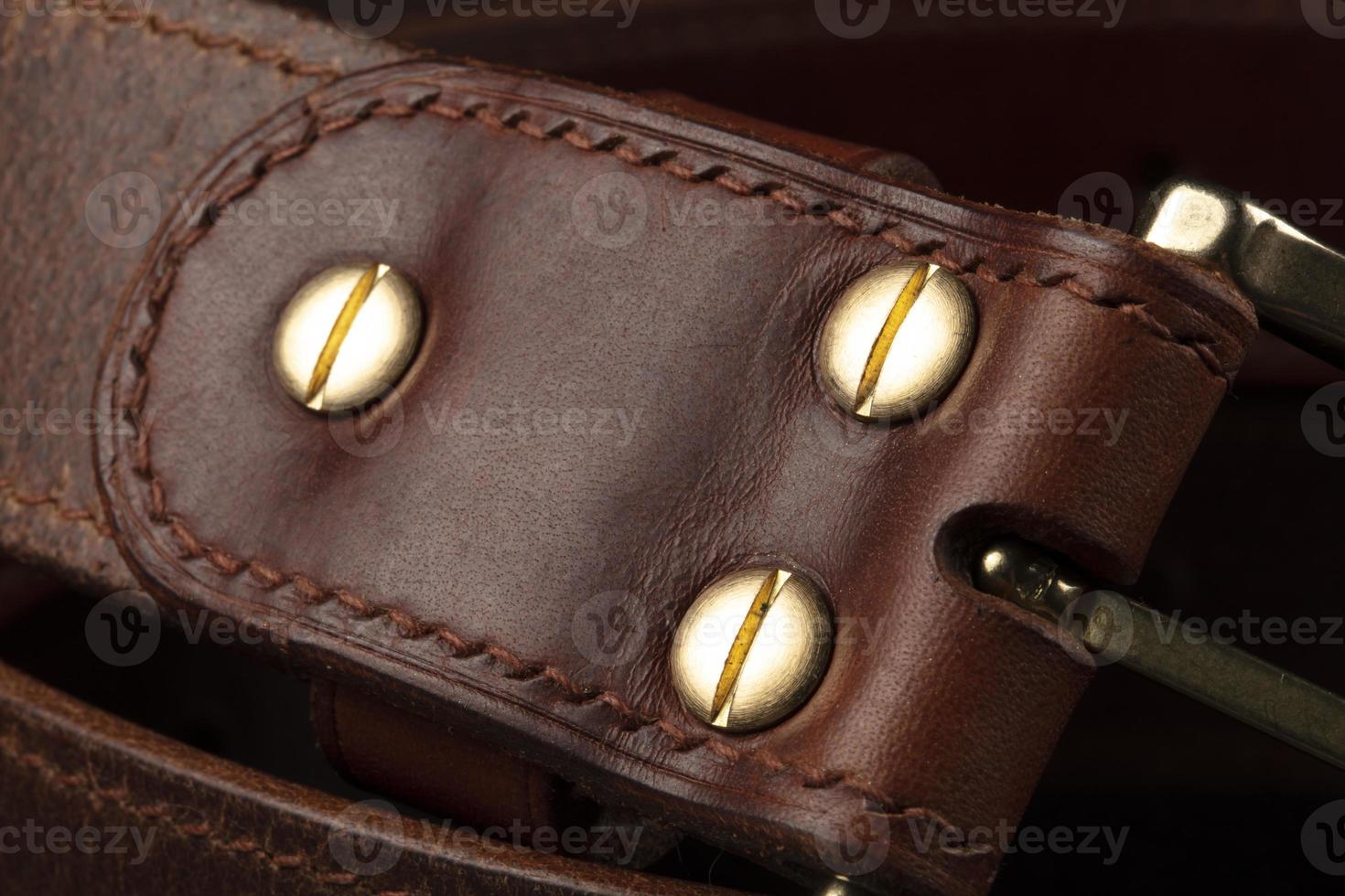 Part of a leather brown belt with a metal buckle on a black background. photo