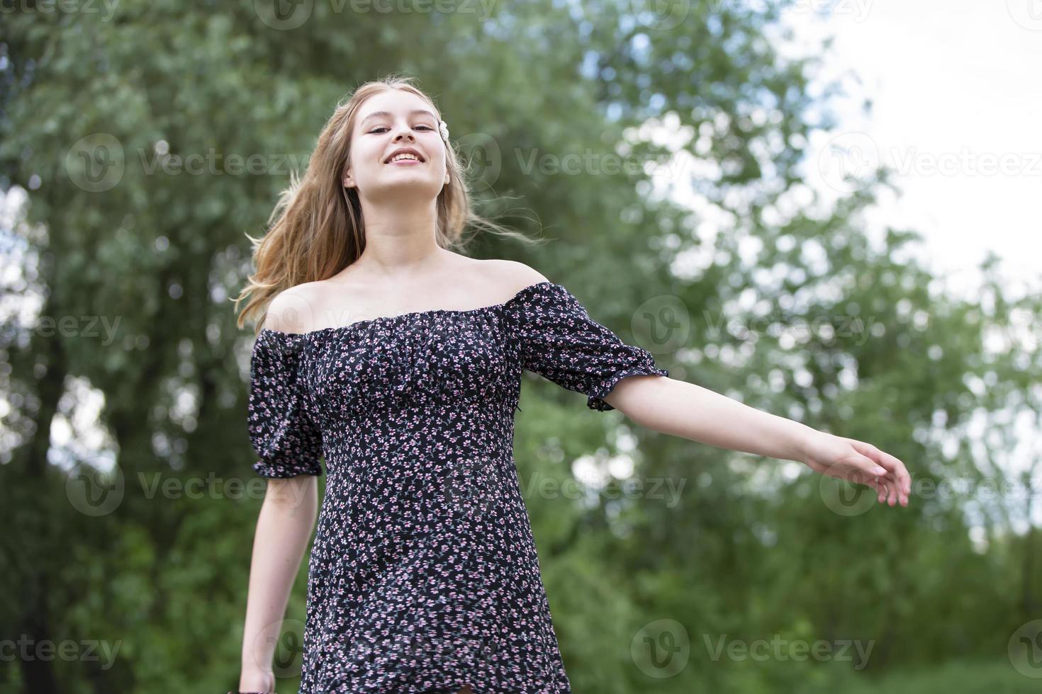 niña feliz en un vestido romántico en un prado verde de verano. hermosa jovencita sonríe y mira a la cámara. foto