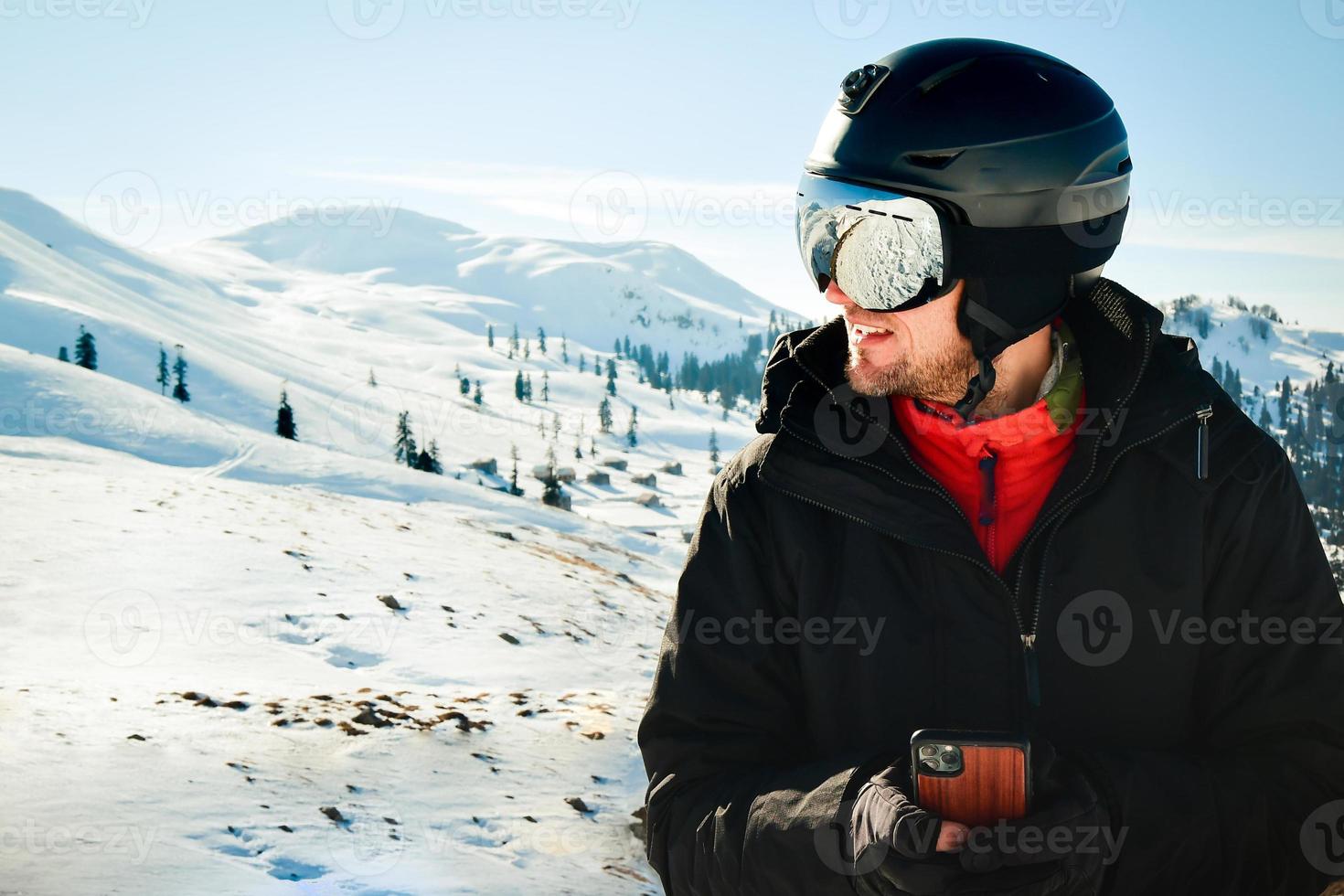 Un esquiador emocionado con chaqueta negra, gafas de esquí, máscara de texto, amigos disparados en el teléfono móvil, pasan el fin de semana de invierno en montañas aisladas en un fondo morado. concepto de hobby de estilo de vida de personas foto