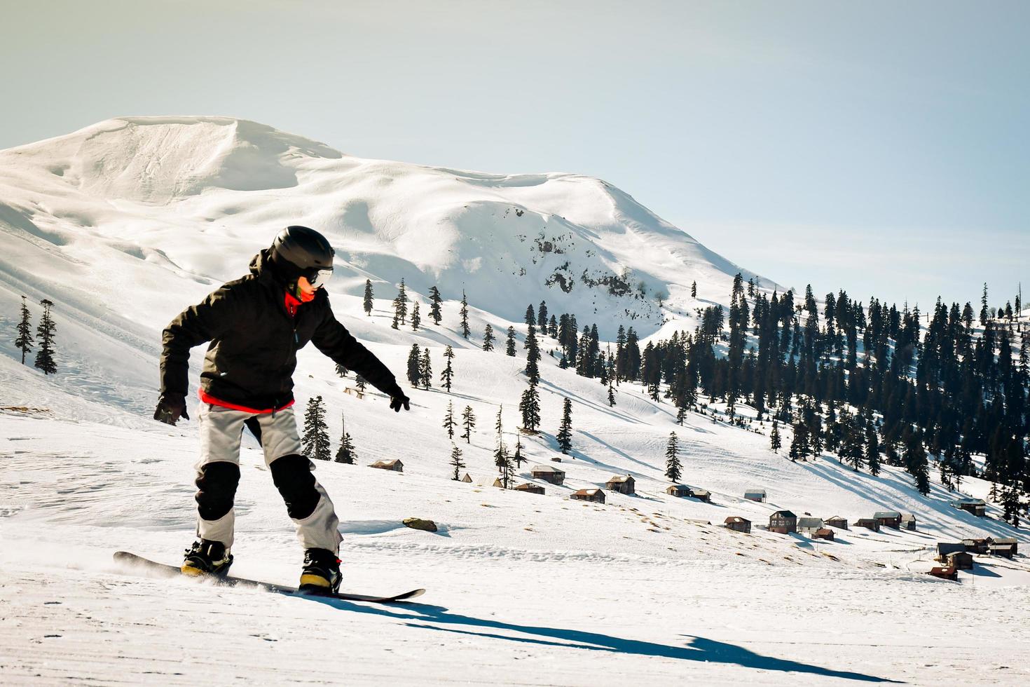 Happy snowboarder dressed in dark black sportswear riding down the mountain slope in Georgia, Goderdzi on caucasus sunny day photo