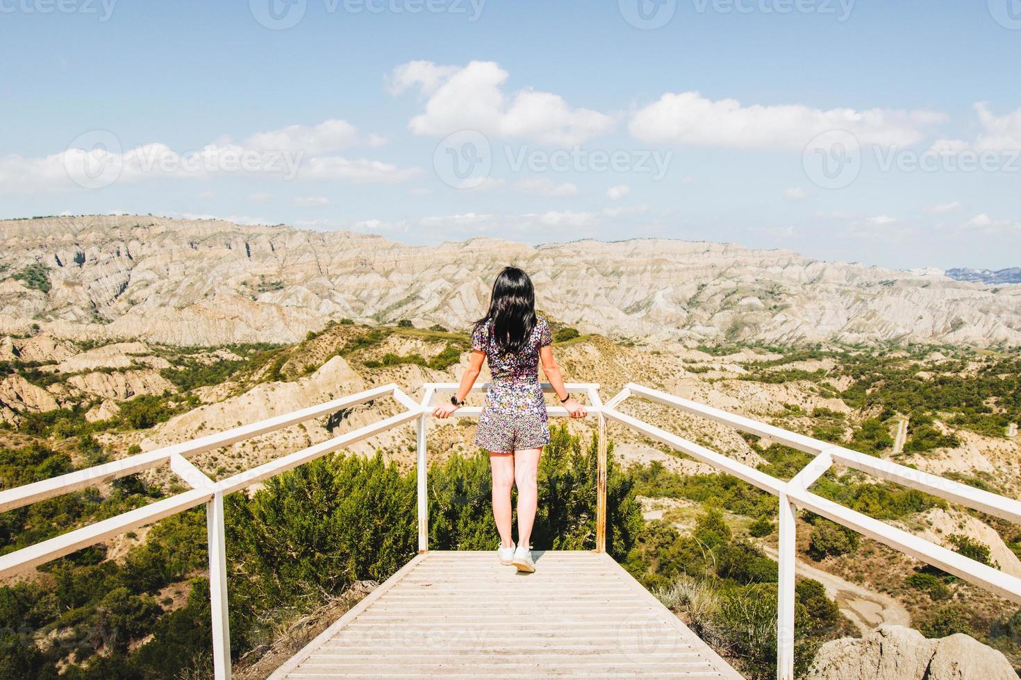 Brunette woman stands on the platform viewpoint and looks left over beautiful landscape of Vashlovani nature reserve photo